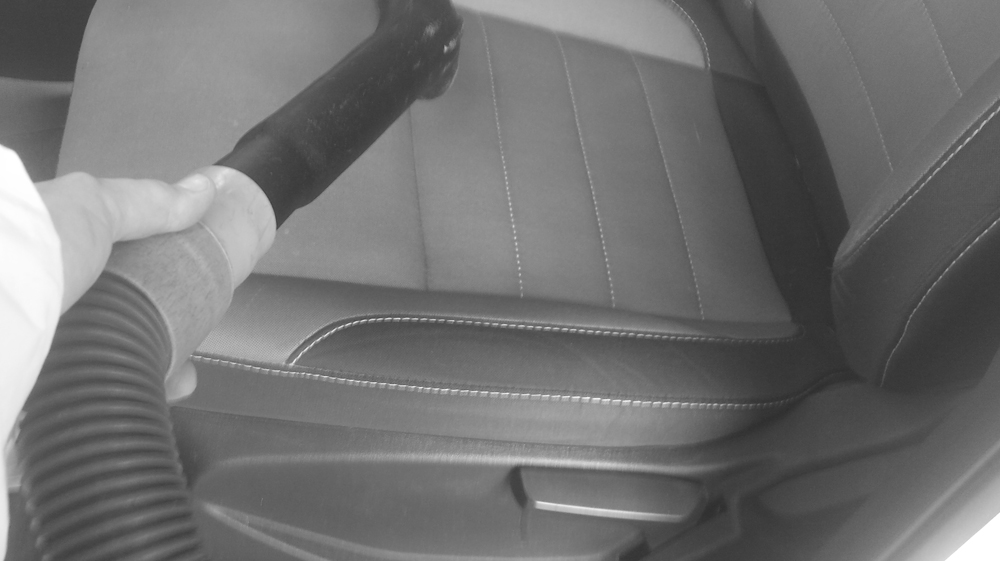 photo of a vacuum hose with a person vacumming a car seat.